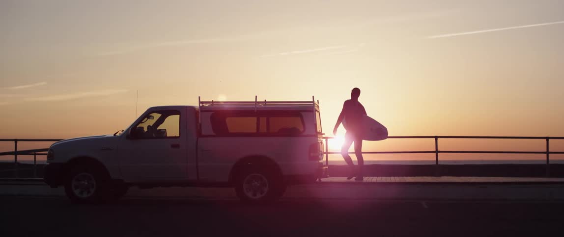A man carries his surfboard towards the beach from the boardwalk