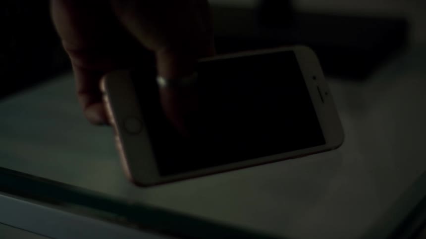 Female uses left hand to pick up smart phone that is sitting on a small table