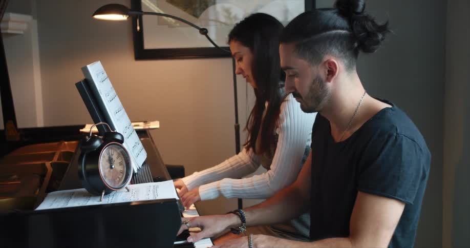 A man and a woman play the piano together