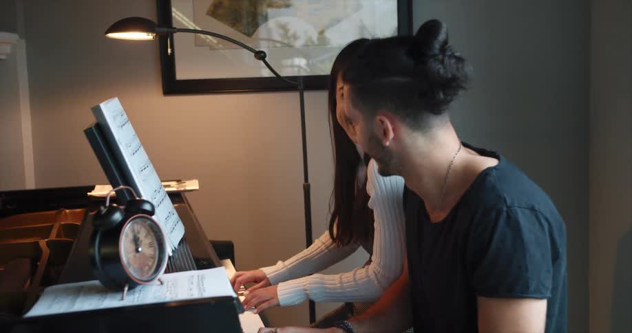 A man and woman laugh as they play the piano together
