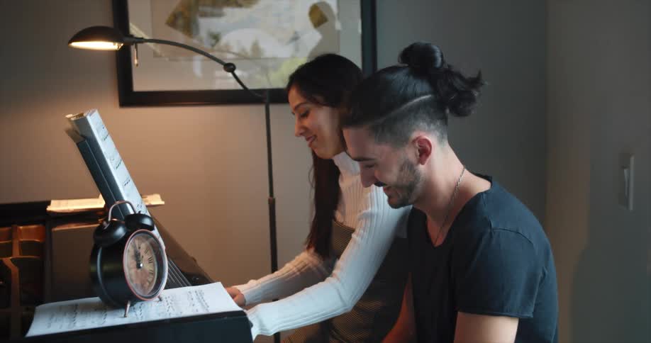 A man and a woman sit at a piano while she plays music