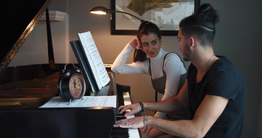 A man plays a grand piano for a young woman