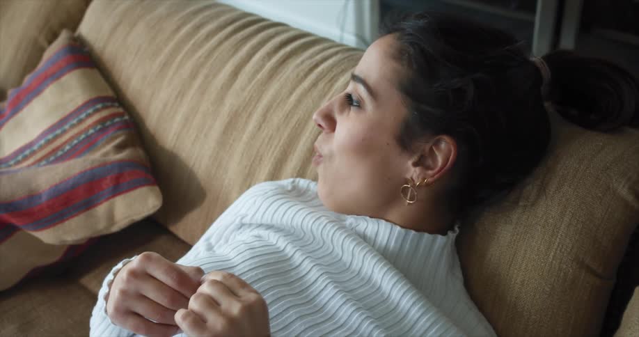 A latina woman in a sweater lounges on a couch while talking and smiling