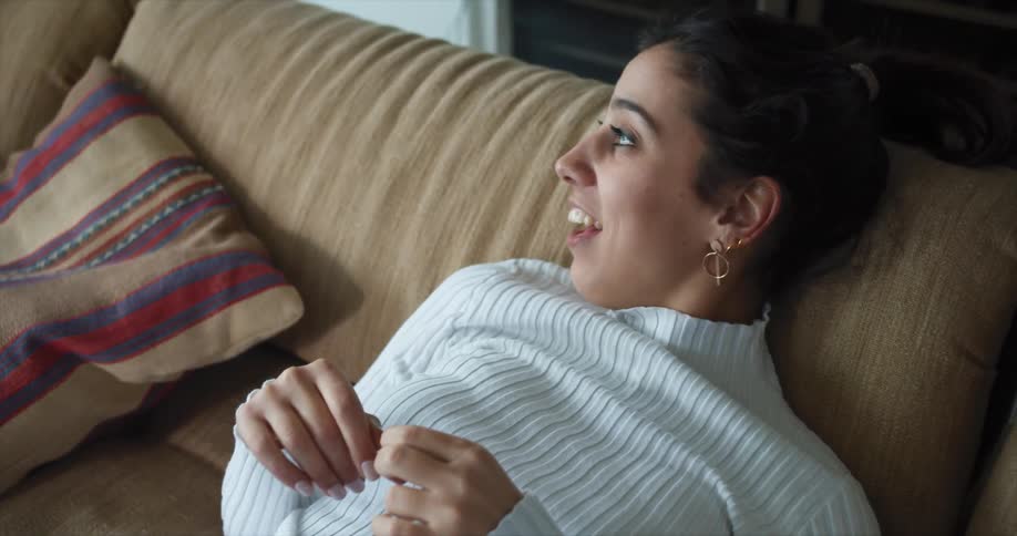 A woman sits on a couch and laughs while seemingly talking to someone else