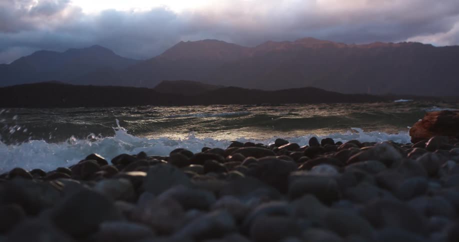 Waves curl and break before splashing on a rocky shore on a cloudy day