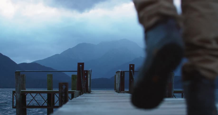 Person walks along pier toward fog covered mountains