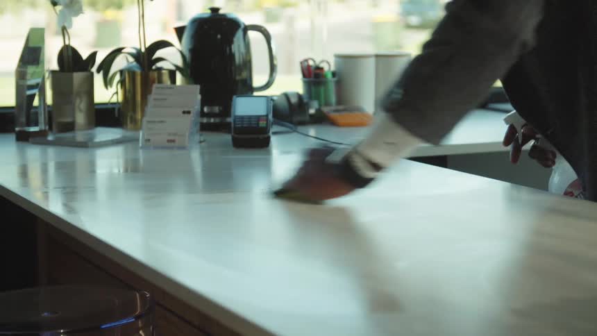 A man with a sponge wiping down a counter with flowers and a window in the background