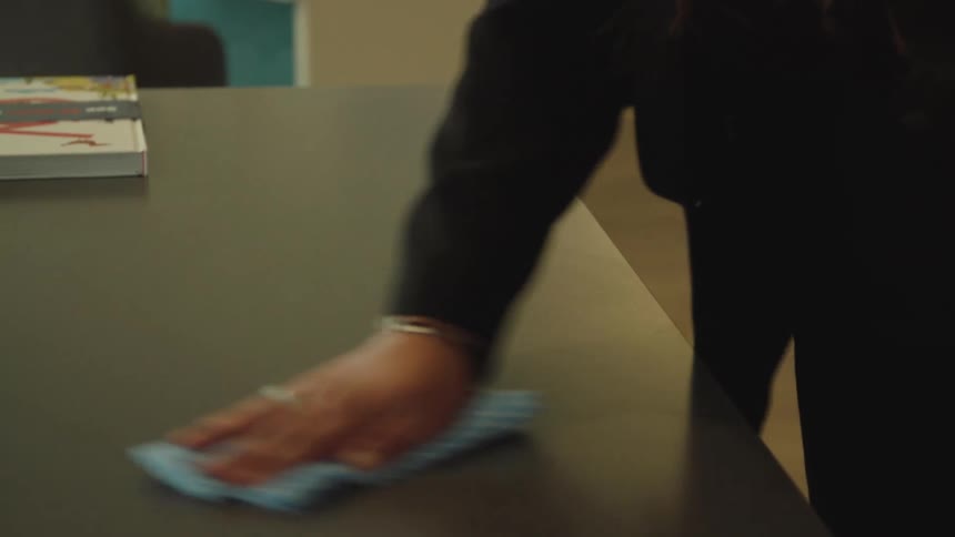 A woman wiping down a desk with a spray cleaner in her hand
