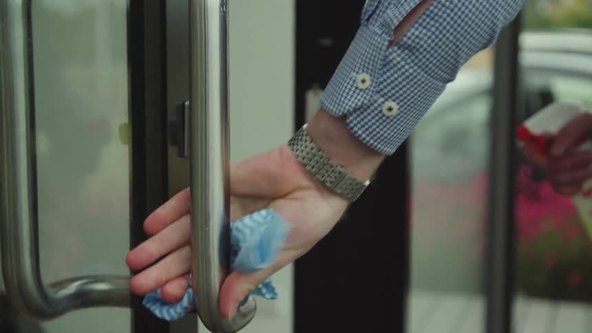 A person with a rag and a spray cleaner cleaning a door handle