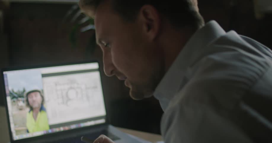 A man talks with a person on the laptop who is on a work site