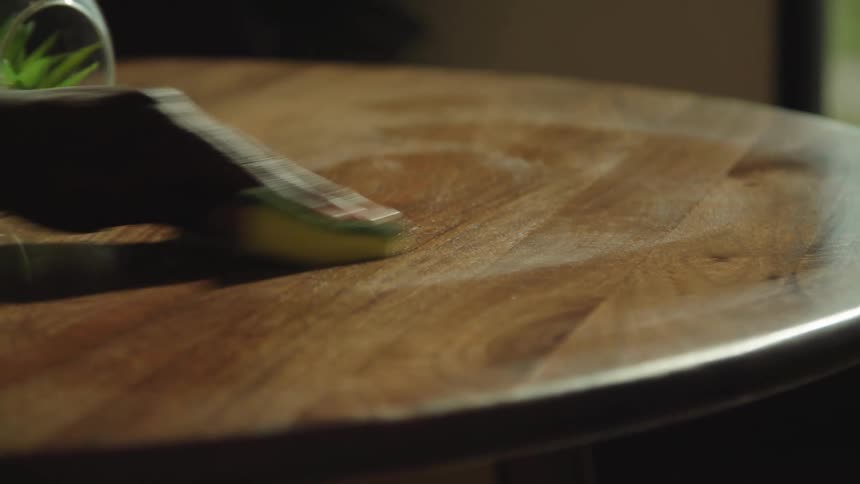 A person wipes the surface of a wooden table with a cleaning sponge