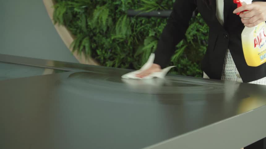 A woman sprays the surface of a counter before wiping it with a paper towel