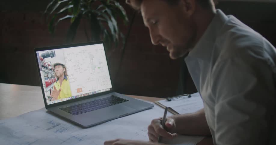 A man looks at a blueprint while talking to another man through video chat on his laptop