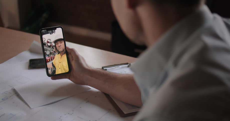 A man sitting at a table holding a smartphone video chatting with another man