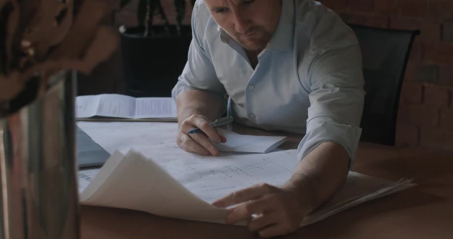 Man sits at desk examining blueprints while voice conferencing