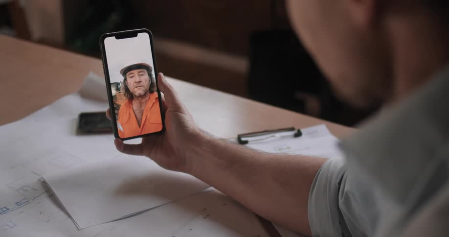 A man sitting at a table holding a smartphone video chatting with a man