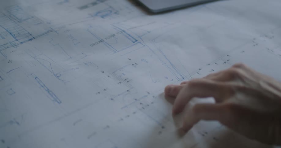A persons hand touching a blueprint next to a laptop