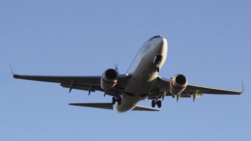 A passenger jet with landing gear down flies in a bright blue sky