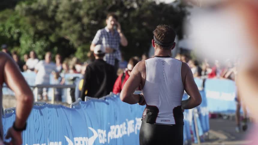 People stand behind a blue banner as marathon runners go by