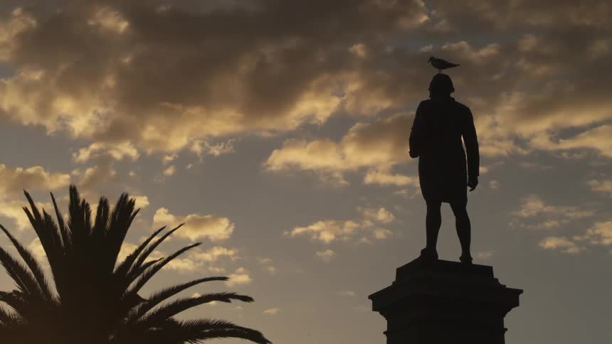 A bird perched upon a statue with the sky and clouds in the background