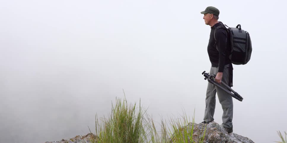 A photographer standing on top of a boulder on a foggy, windy day