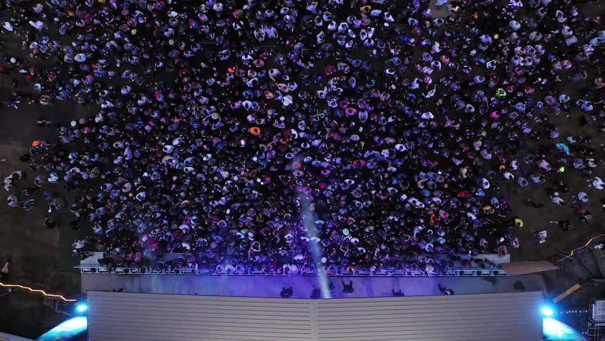 A large crowd of people standing and dancing before a stage emitting flashing blue lights