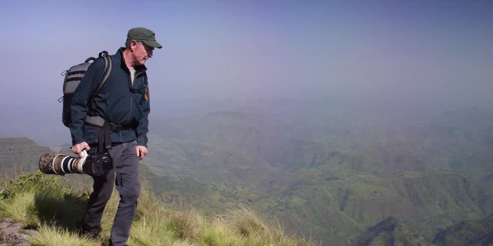A photographer walking along a mountainside