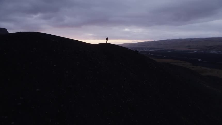 The silhouette of a hiker standing on a mountain while looking out over the countryside below on a cloudy day