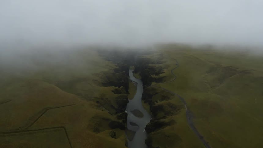 A canyon with a river next to a road with a parking lot with vehicles