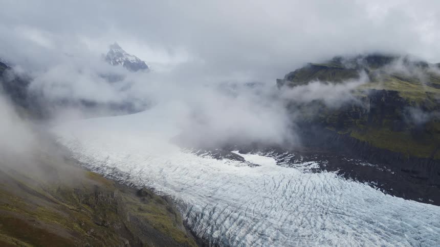Aerial view of clouds covering hills and the icy land below