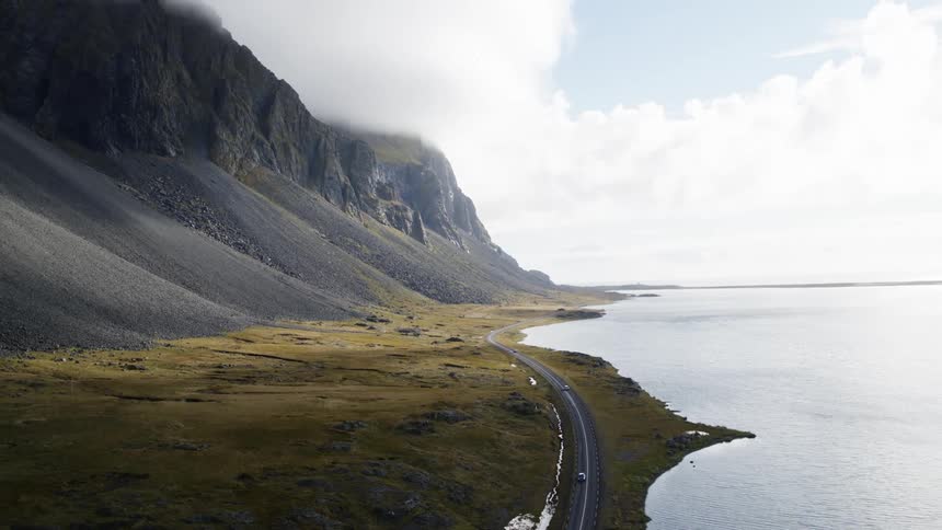 Vehicles traveling along a road between a mountain and the ocean