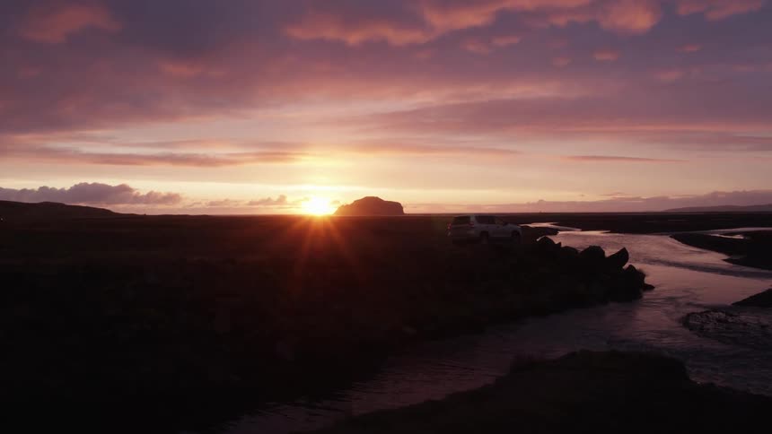 A vehicle next to a river with clouds the sky and a sunset in the background