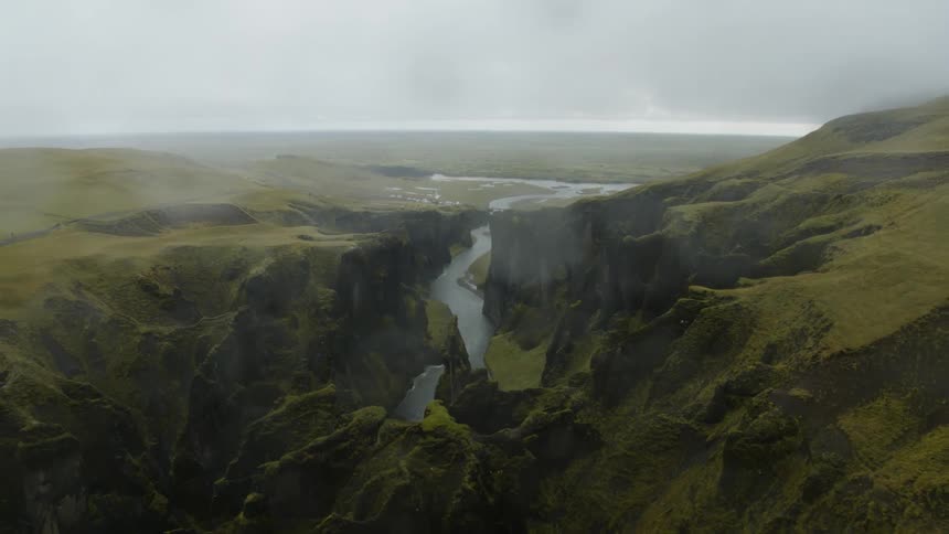 A canyon with a river and fog with the sky and clouds in the background