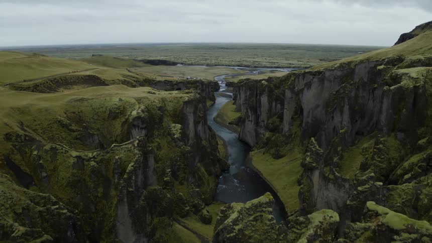 A canyon with a river with a grassy field with the sky and clouds in the background