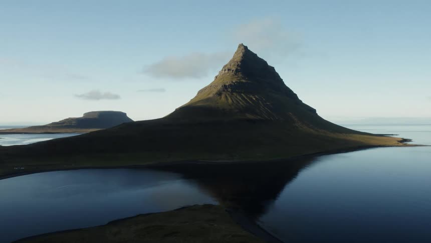 The triangular peak of a rock formation is reflected in the smooth blue surface of the water