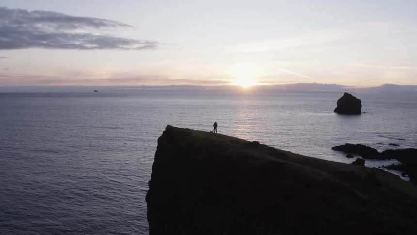 A person setting up equipment on a tall stone promontory on the coast