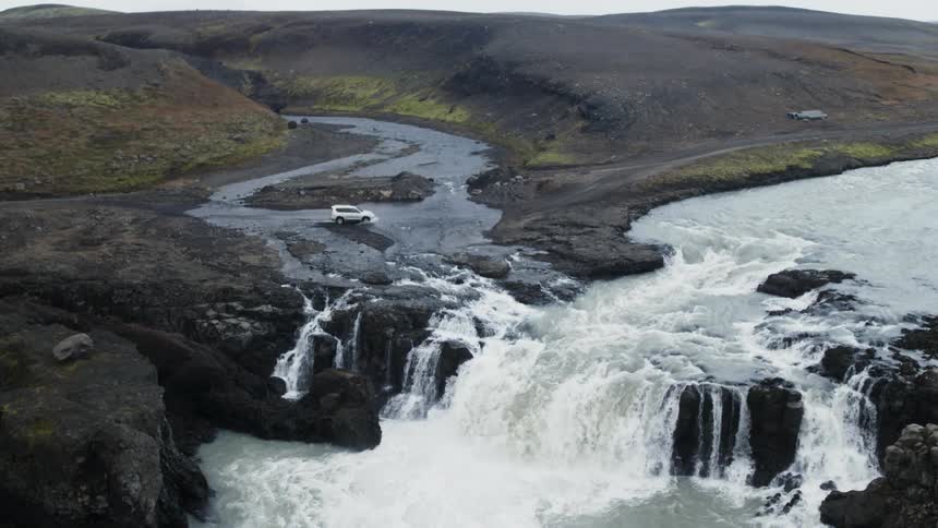 A suv travels off road through a stream and into a muddy path next to a waterfall