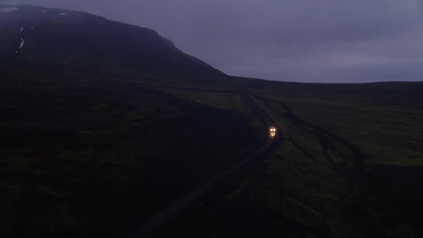 A vehicle travels through the darkness along a road through a vast grassland