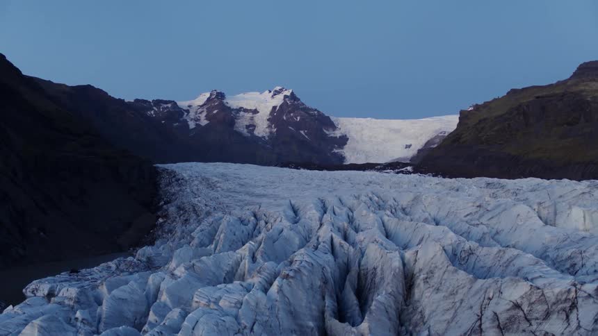 An icy glacier with a snow covered mountain rangeand the sky in the background
