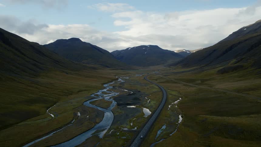 A vehicle drives down the road between the hills