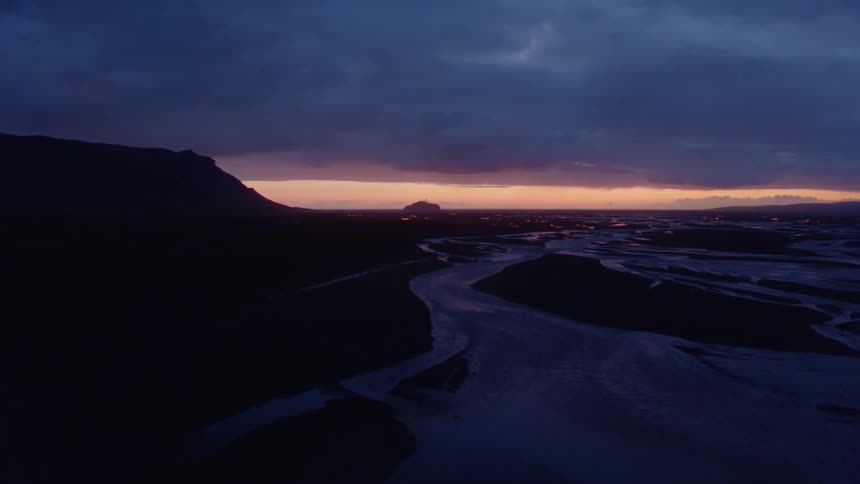 Winding waterways flow past mountain toward town and red overcast sky