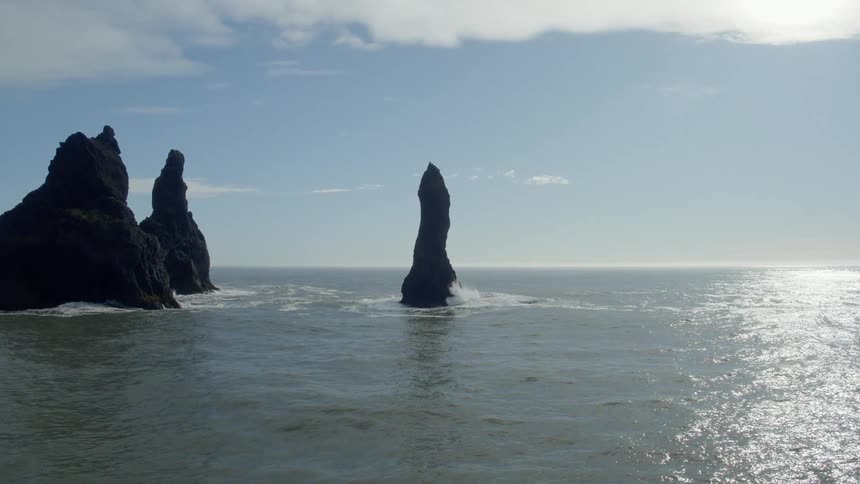 An ocean with three rocks jutting out the water with the sky and clouds in the background
