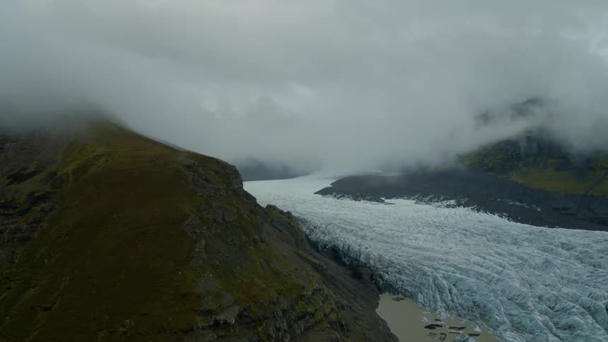 A glacier next to a cliff with fog with the sky and clouds in the background
