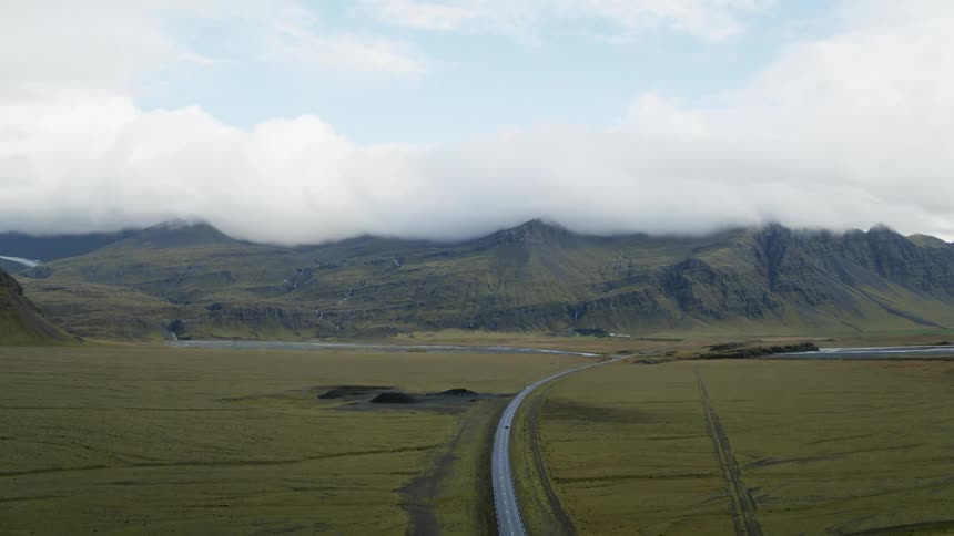 A vehicle travels along a road through a vast grassland between mountain ridges