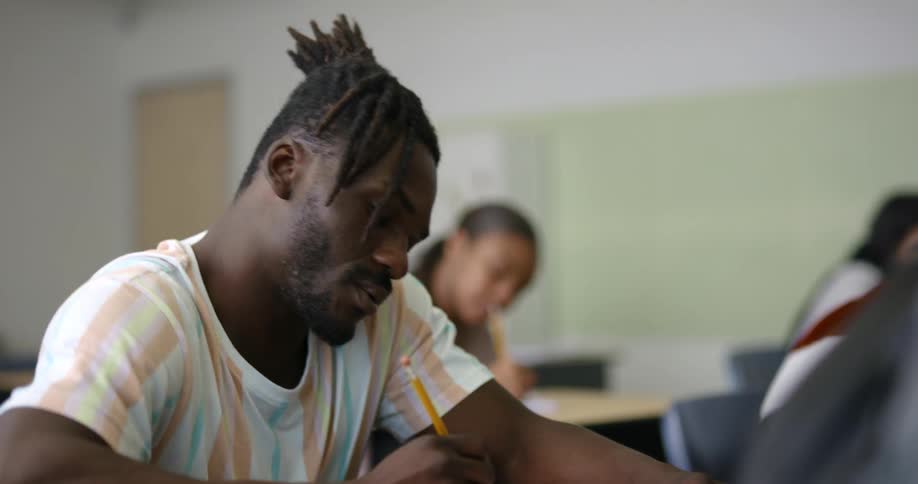Students sit at desks in classroom writing on paper