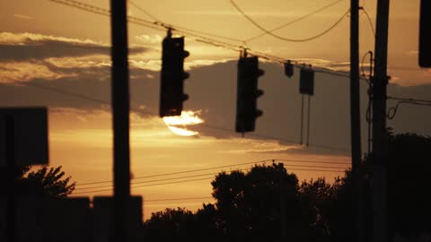 The silhouette of traffic lights poles and wires against a golden sky at sunrise