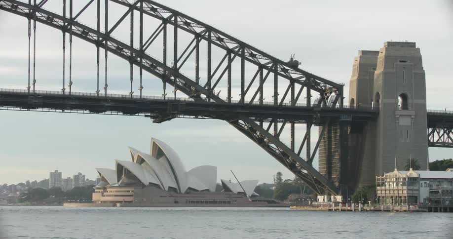 A bridge over water with a opera house and buildings in the background