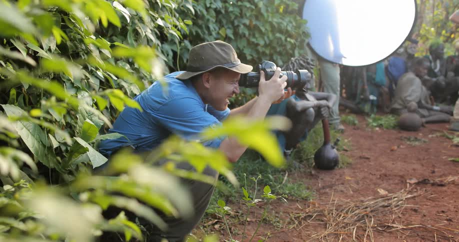 A man is crouching near a bush using a camera