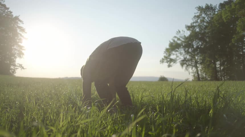 A man stretching on a grassy field with the sky and the sun in the background
