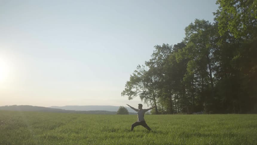 A man does yoga outdoors in a field on a sunny day